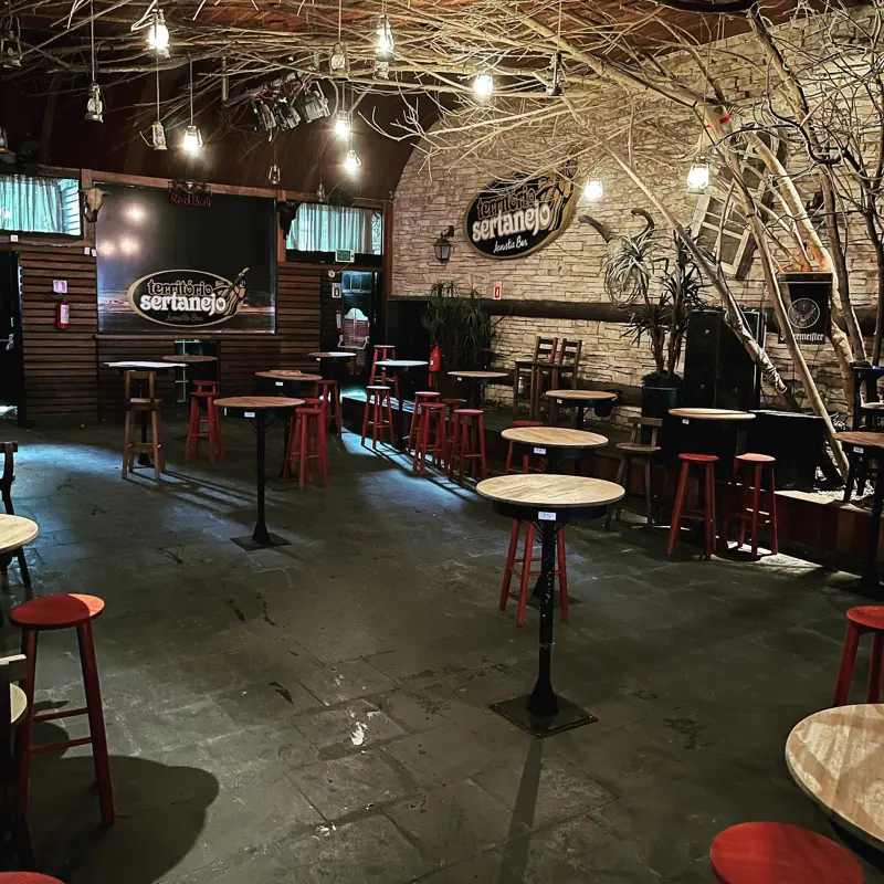 Salão do Bar Território Sertanejo com mesas altas, palco e decoração rústica